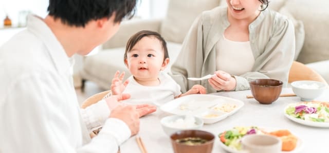乳幼児と若い夫婦の家族が明るい食卓を囲む様子